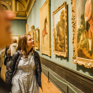 Visitor admiring a series of framed paintings in a richly decorated gallery room at the National Gallery.