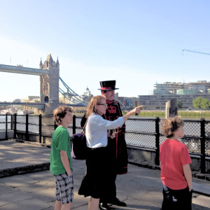 Family group listening to a Beefeater guide pointing out views by the River Thames, with Tower Bridge in the background.