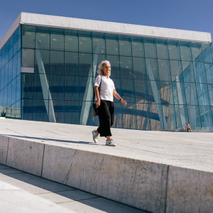 A woman walking along the sloped white marble roof of the Oslo Opera House on a sunny day.