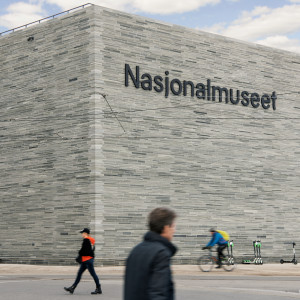 Modern gray stone building with “Nasjonalmuseet” on the facade as people walk and cycle past.