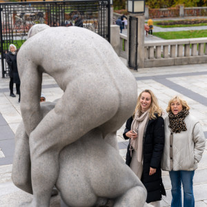 Two women admire granite statues in Vigeland Park on a cool autumn day.