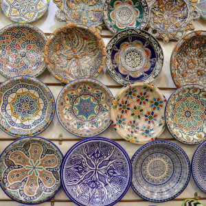 A wall display of hand-painted Moroccan ceramic plates, each decorated with intricate geometric, floral, and calligraphic patterns in vivid blues, greens, and earth tones.