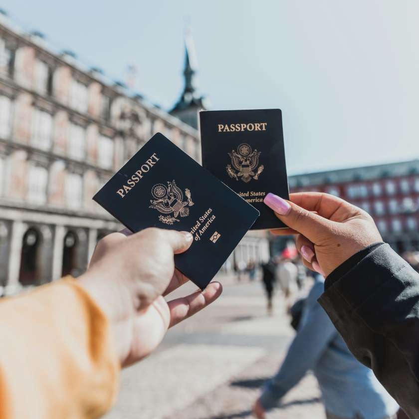 two hands holding american passports with a European plaza in the background