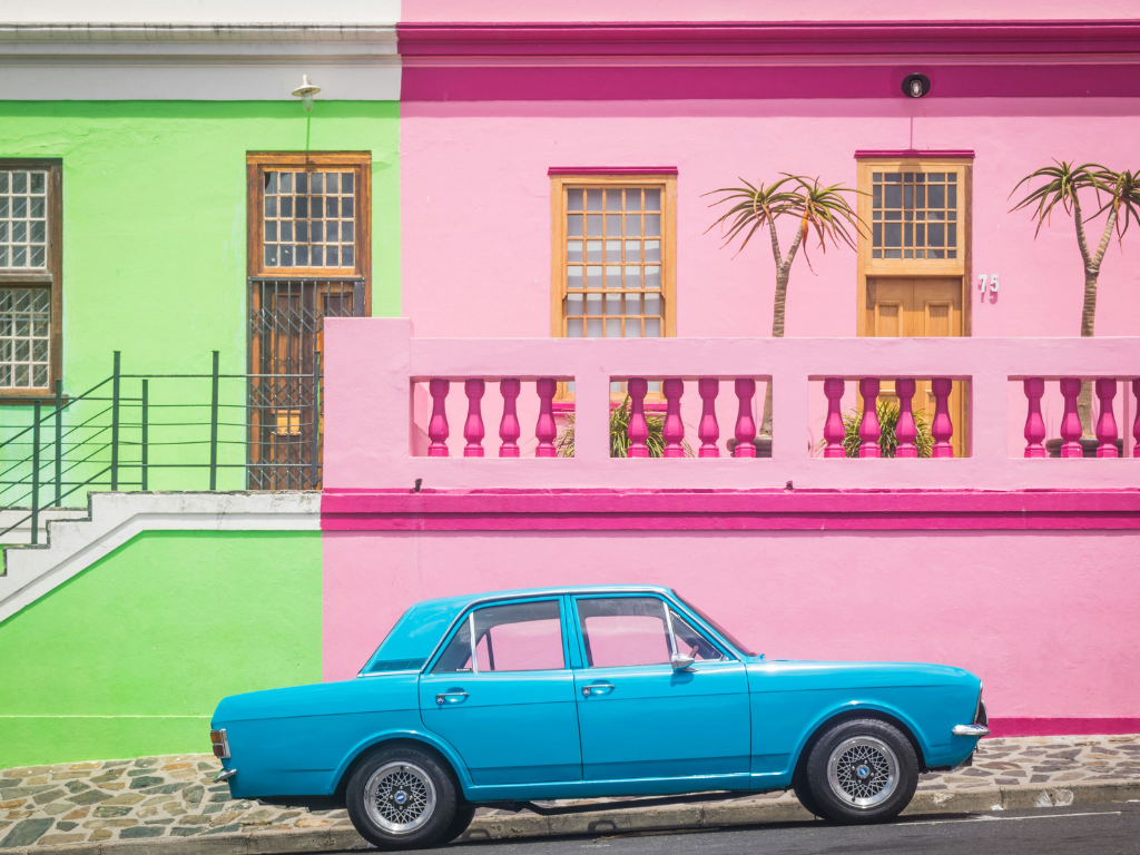 A neon green house next to a bright pink house, with a small bright blue car parked in front.