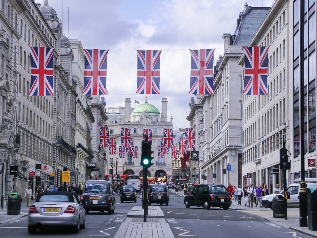 A busy street in London with many cars, the multiple UK flags strung above the street