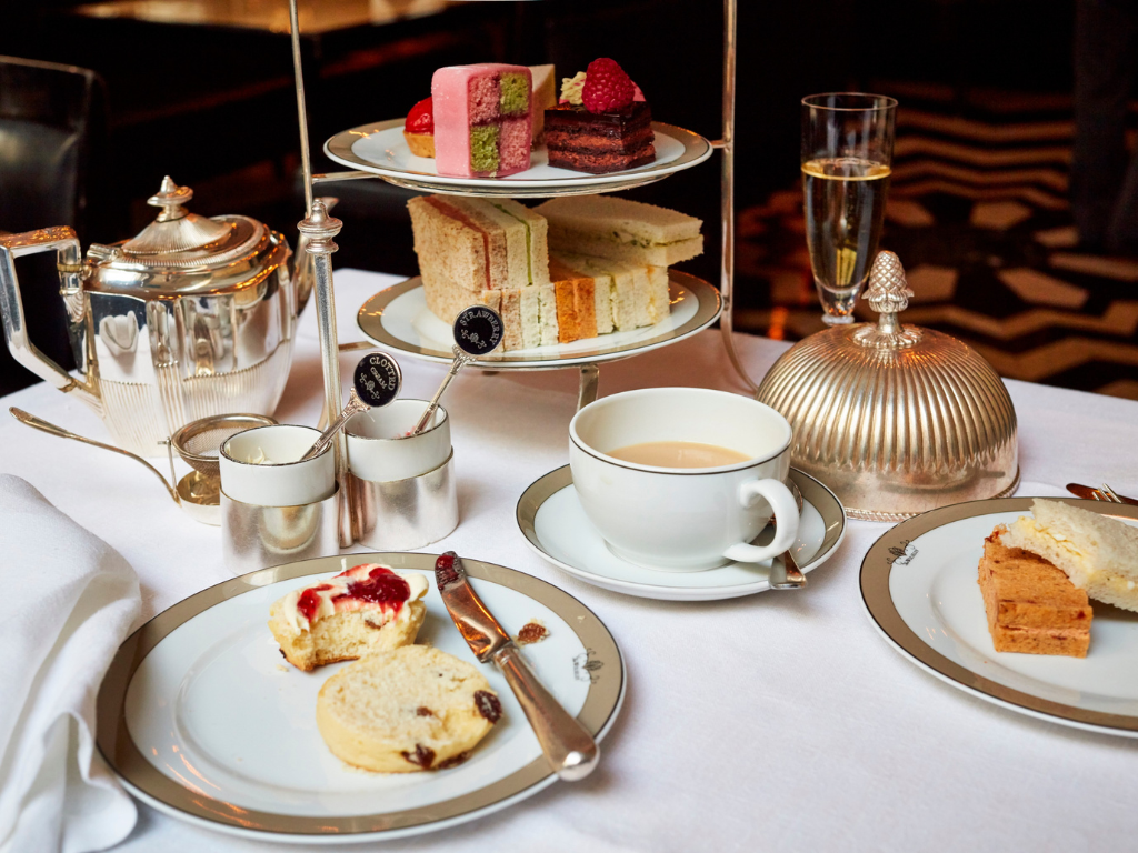 A tray with sandwiches and desserts, tea, and a plate with butter and jam biscuit