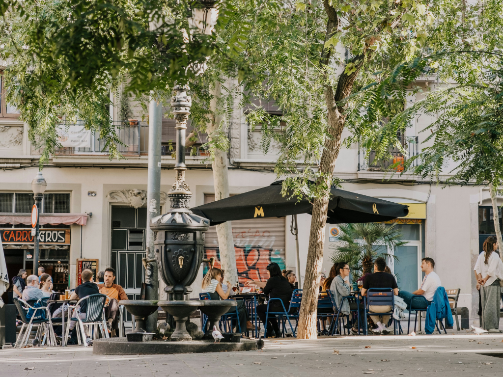 A group of people sitting at a table on a shaded patio under an umbrella in Barcelona