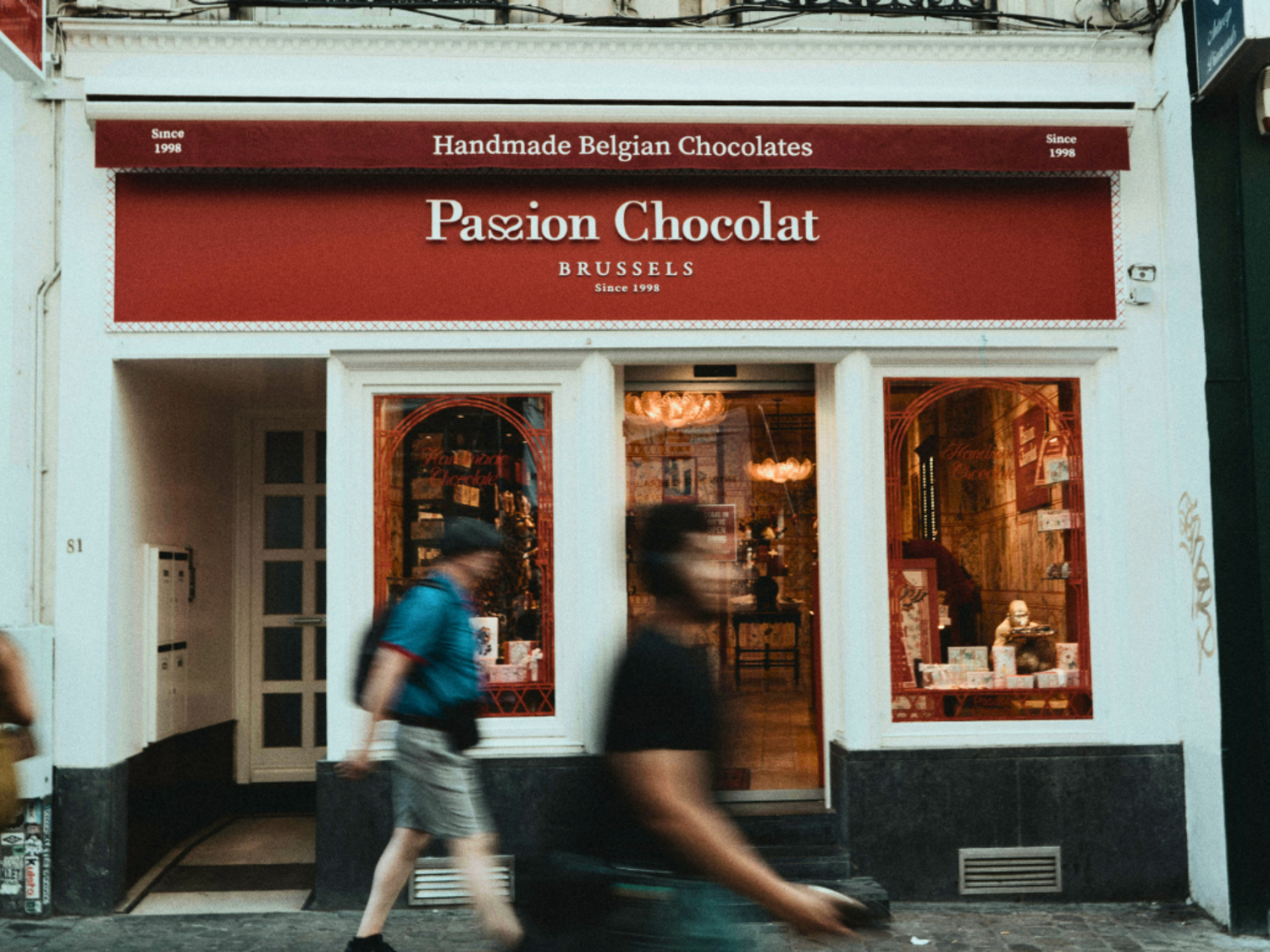 The storefront of Passion Chocolat in Brussels, passersby blurred in long exposure in front of the shop.